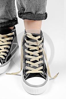 Sneaker with untied laces on a female leg on a white background