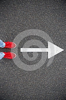 Sneakers on the asphalt road with drawn direction arrow