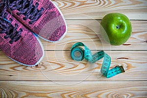 Sneakers, centimeter and fresh apple top view. Healthy and active lifestyles. Wooden background.