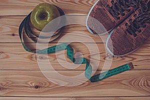 Sneakers, centimeter and fresh apple top view. Healthy and active lifestyles. Wooden background.