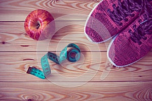 Sneakers, centimeter and fresh apple top view. Healthy and active lifestyles. Wooden background.