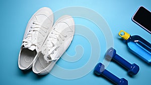 Sneakers, dumbbells, smart phone and bottle of water on blue background.