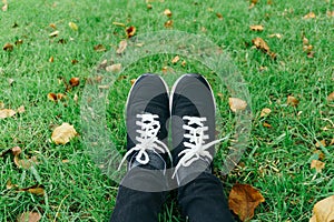 Sneakers on girl legs on grass during sunny serene summer day.