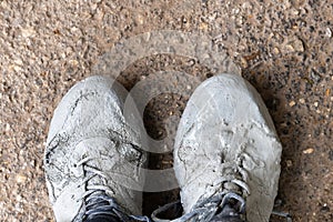 Sneakers heavily stained in grey paint on an asphalt
