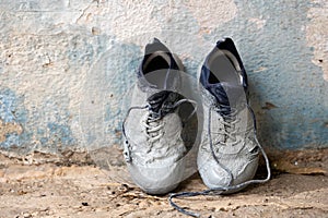 Sneakers heavily stained in grey paint are standing against the wall