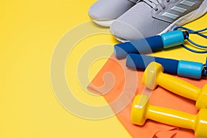 Sneakers, jump rope, dumbbells and mini-band for sports and fitness on a yellow background with copy space.