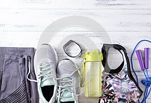 Sneakers, leggings, top, jump rope, water bottle, sports bracelet, sportswear on a white wooden background