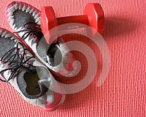 Sneakers and a red dumbbell put on a yoga mat.