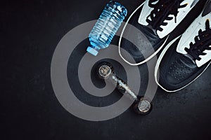 Sneakers, water bottle and dumbbell on dark background with copy space, exercise concept