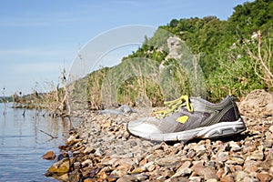 Sneakers with yellow laces near the water, beach with stones.