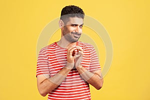 Sneaky cunful man with beard in striped red t-shirt drumming fingers planning devious pranks, thinking over revenge plan, scheming