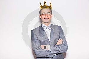 Sneering young handsome man wearing suit and crown keeping arms crossed