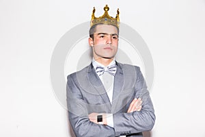 Sneering young handsome man wearing suit and crown keeping arms crossed photo
