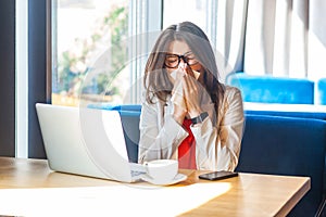 Sneeze, cold, influenza or allergies. Portrait of sick stylish brunette young woman in glasses sitting holding tissue napkin and