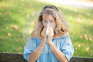 sneezing young girl with nose wiper in park