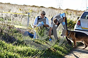 Sniffing out a suspect. Shot of two investigators taking notes while examining a body at a crime scene.