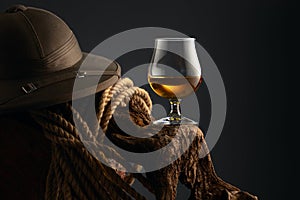 Snifter of brandy, cork tropical colonial helmet and rope on a old wooden snag