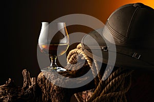 Snifter of brandy, cork tropical colonial helmet and rope on a old wooden snag