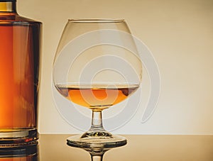 Snifter of brandy in elegant typical cognac glass near bottle on table, warm style