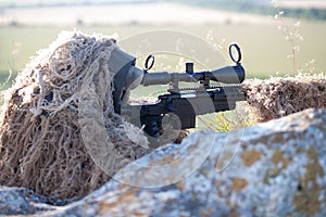Sniper in ghillie suit with precision rifle with optic sight
