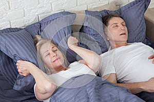 Snoring man. Couple in bed, man snoring and woman can not sleep, covering ears with pillow for snore noise. Middle age