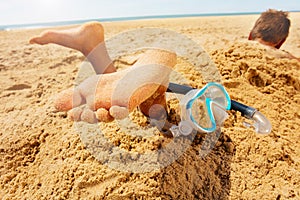 Snorkel, mask and boy feet buried in sand beach