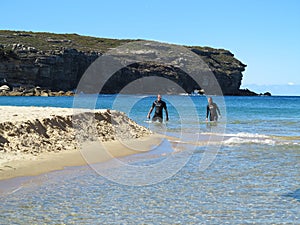 Snorkeling couple wade out of water in bay landscape