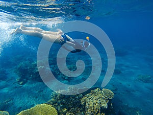 Snorkeling girl in full-face snorkeling mask. Coral reef in shallow sea.