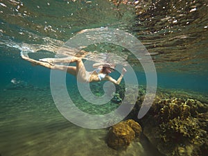 Woman is swimming diving among coral reefs in shallow water and looking underwater sealife.