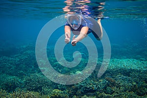 Snorkeling woman in full face mask. Underwater coral landscape and snorkel.