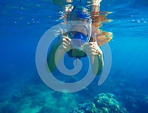 Snorkeling woman underwater showing thumbs. Snorkel in full face mask.