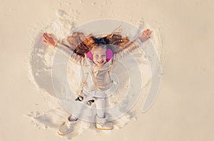 Snow angel made by a kid in the snow. Smiling child lying on snow with copy space. Funny kid making snow angel.