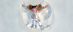 Snow angel. Smiling child lying on snow with copy space. Funny kid making snow angel. Happy kid girl make snow angel