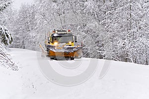 A snow blower car clears snow in the forest from the road on a winter morning. Snow plow truck cleaning icy white road