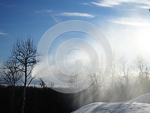 Snow cannon. Snowmaker in action at ski resort spraying artificial snow with mountains in background. Snow that is reflected in