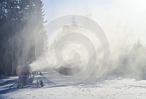 Snow cannon in winter mountains. Snow-gun spraying artificial ice crystals. Machine making snow.