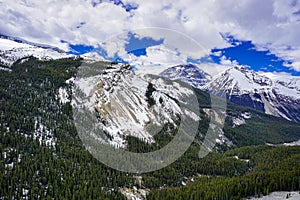 Snow capped Canada`s Rockies mountain during a summer day contrasting with a bright blue sky and white clouds