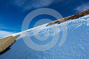 Snow-capped hillside in sunshine under a cloudy, deep-blue sky.