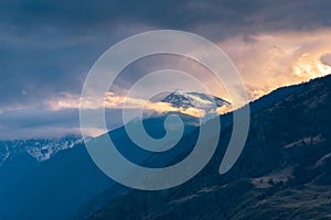 Snow-capped mountain glowing in sunset light with dramatic clouds and fog in Cawston, British Columbia, Canada