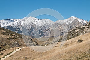 Snow-capped mountains lie at the end of a path through rocky hillsides