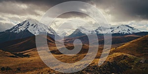 Snow-capped mountains with small hills in front of them. A heavy sky overhangs the scenery