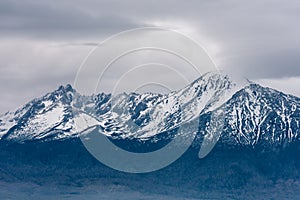 Snow-capped peaks of rocky mountains with overcast gray sky
