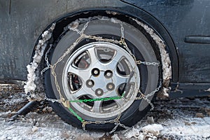 Snow chains on a car wheel. The fenders of the car are forgotten by the muddy snow. The concept of safety on snowy roads