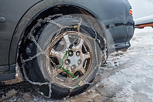 Snow chains on a dirty snowy car wheel. Close-up. The concept of safety on snowy roads.