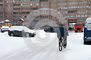 Snow cleaner rides a bike in the snowfall. Against the background is snow plow. The problem of snow removal