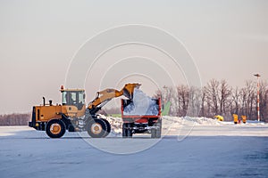 Snow cleaning in airport. Excavator loads snow into dump truck