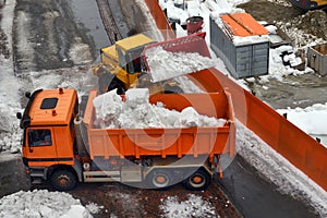 Snow cleaning tractor snow-removal machine loading pile of snow on a dump truck