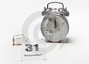 A snow-covered alarm clock and a loose-leaf calendar with the date December 31