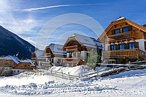Snow-covered alpine chalets under bright winter sun with mountains in the background
