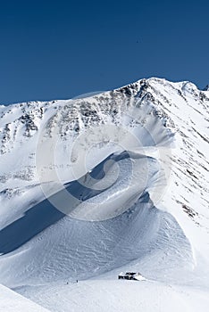 Snow covered alpine mountain hut with two skiers in winter